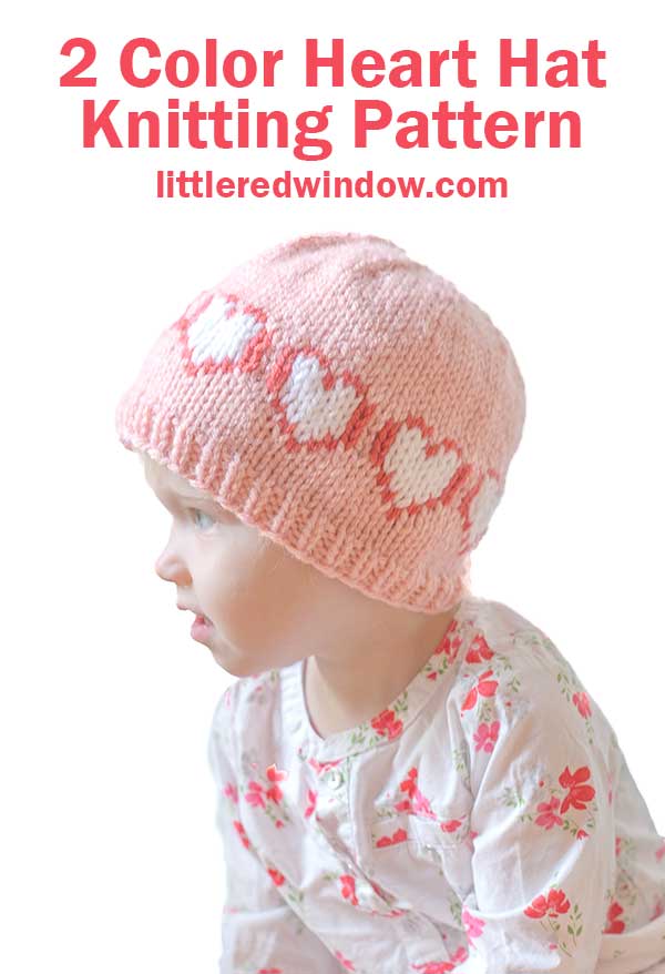 A child wearing a pink Heart Hat adorned with charming white and pink heart patterns sits in profile, dressed in a delightful floral-patterned outfit. Text above reads,