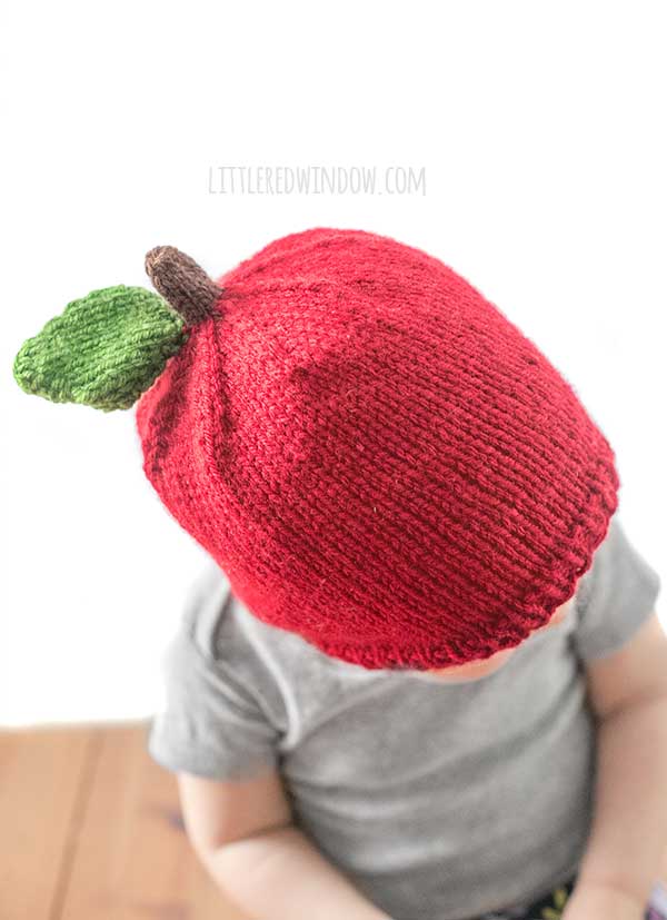 top view of baby in gray shirt wearing a red knit hat that looks like an apple