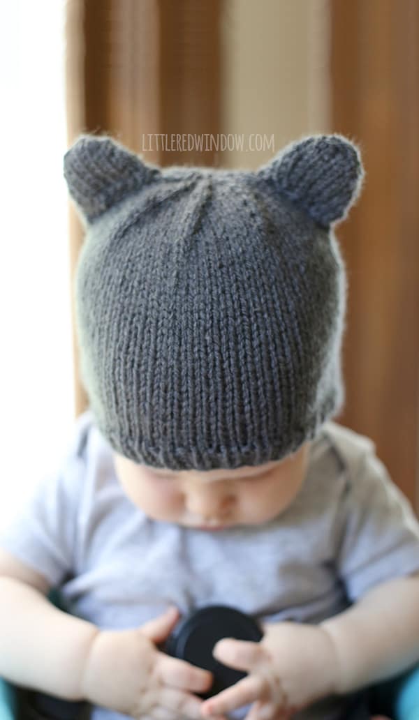 closeup of Baby holding a lens cap and wearing a knit hat with bear ears and looking down at their hands