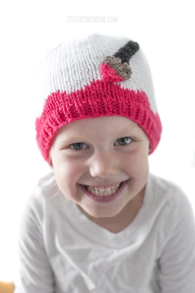 Little girl smiling big and wearing a white hat with pink along the brim and an applique paintbrush painting on the pink