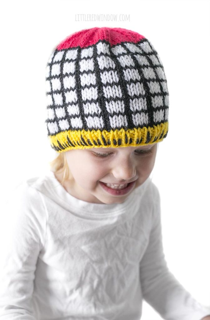 Little girl wearing knit hat with black and white grid and yellow ruler brim
