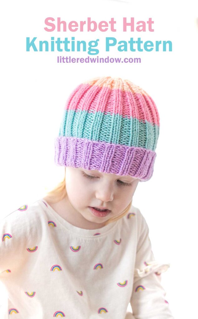 A young child wearing a colorful knitted hat with pink, blue, and purple stripes, paired with a white shirt adorned with small rainbow graphics. Above the child, the text reads, 