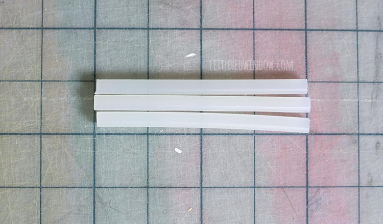 3 four inch long white mini hot glue sticks on a gridded cutting mat