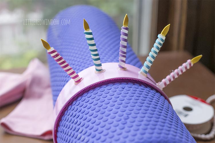 6 hot glue stick candles attached to the top of a pink plastic headband which is held by a purple foam roller finished headpiece for the birthday cake costume