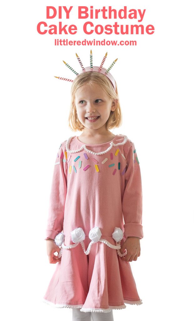 girl in pink birthday cake dress with sprinkles and white frosting rosettes smiling and standing on a table