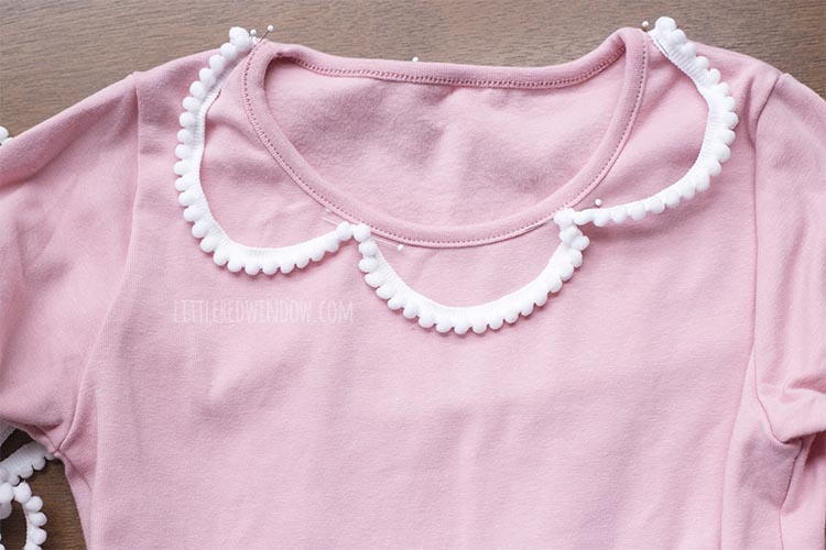 pink dress with white pom pom trim swagged around the neckline