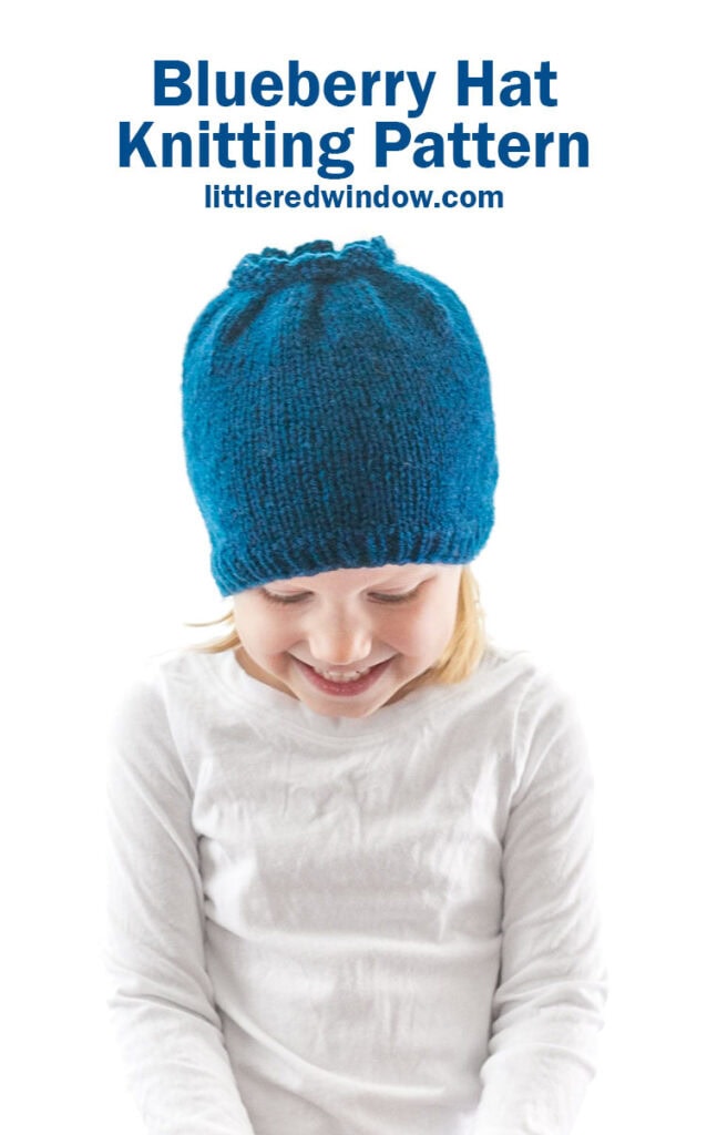 little girl in white shirt looking down and wearing a blue knit hat that looks like a blueberry
