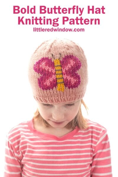 A young girl in a pink and white striped shirt wears a knitted hat featuring a bold, pink butterfly design. Above her, the text reads: "Bold Butterfly Hat Knitting Pattern littleredwindow.com".