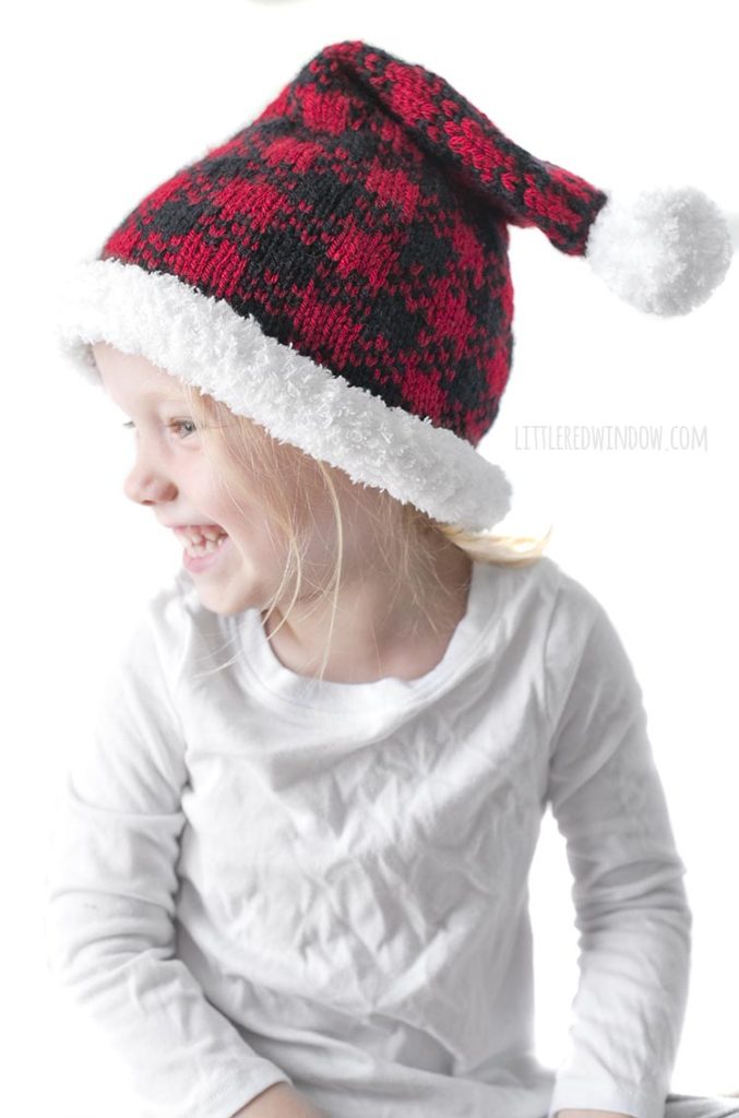 little girl wearing red and black buffalo plaid santa hat and looking off to the left