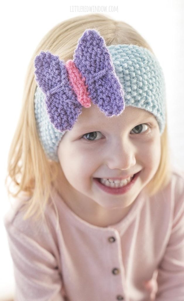 Closeup of girl smiling and wearing blue knit headband with purple and pink butterfly on the front