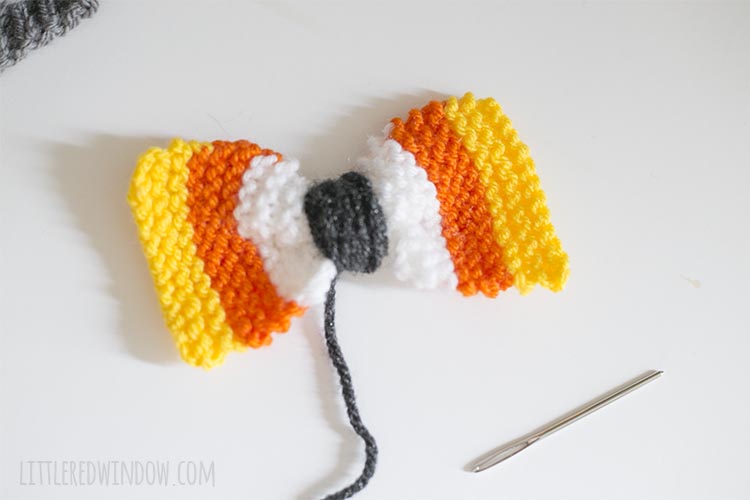 knit candy corn stripe rectangle with charcoal yarn wound around the center to make a bow