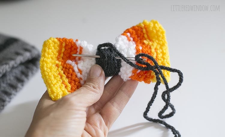 hand holding bow with yarn needle inserted through the center knot to secure the yarn