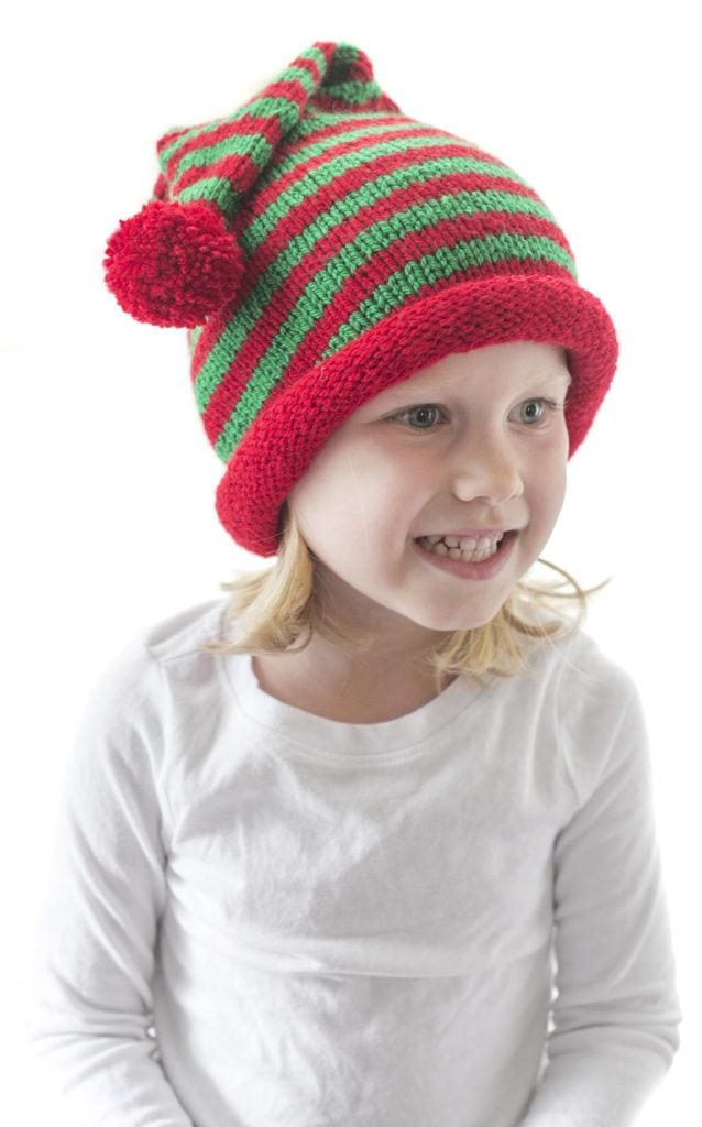 little girl looing off to the right and wearing a red and green striped stocking cap with rolled brim and red pom pom