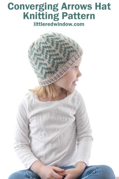 little girl looking off to right and wearing tan and teal coverging arrows hat knitting pattern