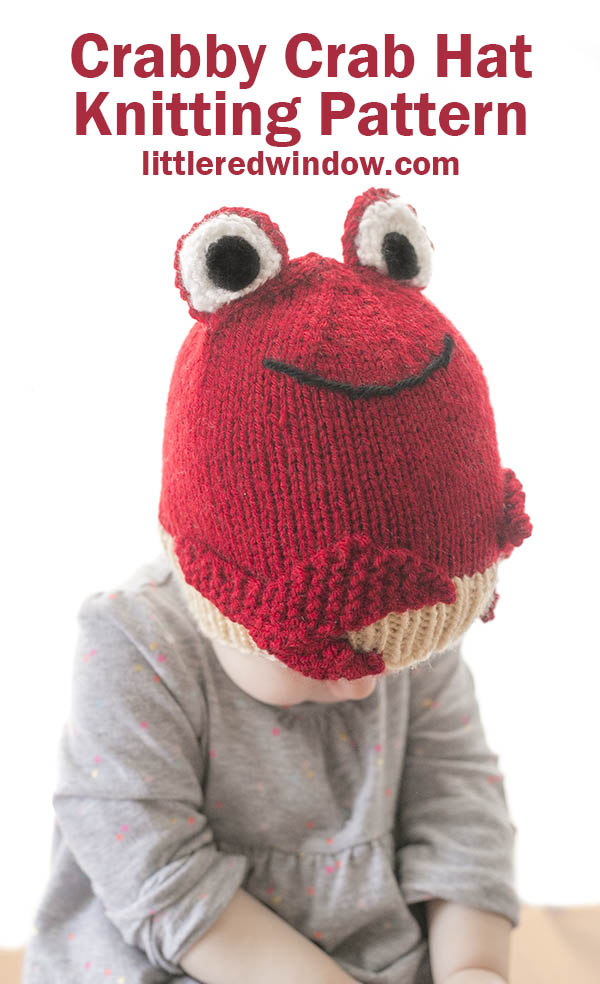 little girl in gray shirt wearing a red knit hat that looks like a red crab looking down at her lap
