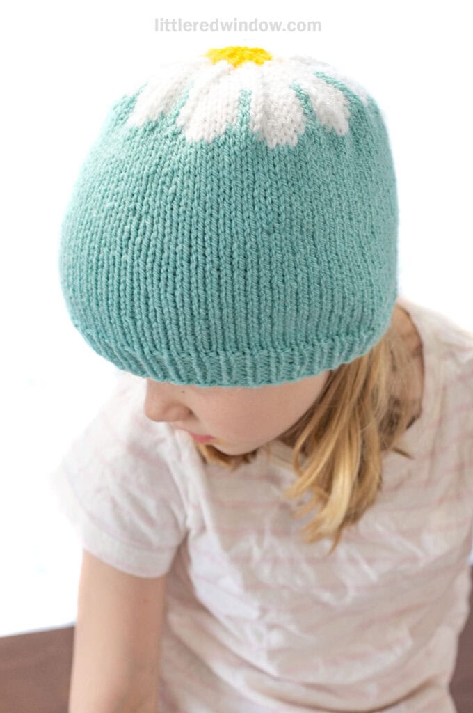 view from slightly above of child wearing blue knit hat with daisy on top looking down and to the left