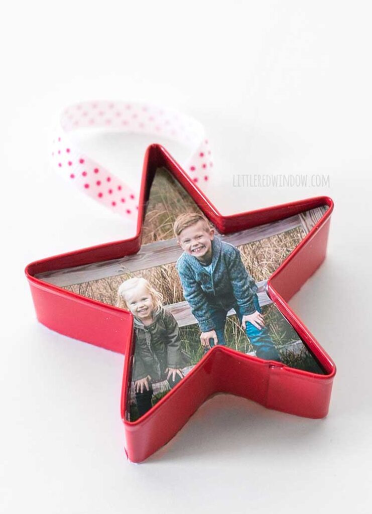 close up of a red cookie cutter ornament with a photo of two children in side and a ribbon hanging loop on a white background