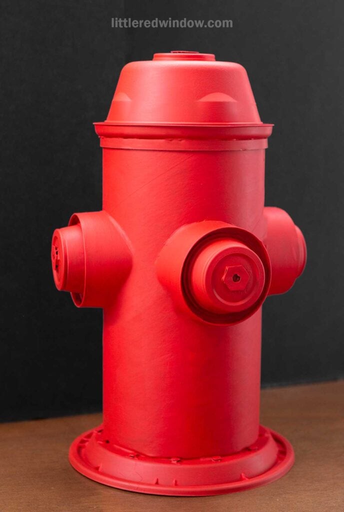 A bright red fire hydrant against a dark background, featuring two side nozzles and a domed top. The hydrant is clean and prominently positioned.
