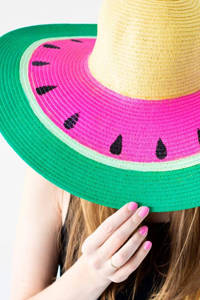 Straw sun hat with the brim painted with green white and pink stripes and black seeds to look like a watermelon
