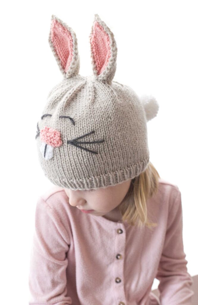view from slightly above of child wearing funny bunny hat with knit bunny ears cute bunny face and fluffy bunny yarn pom pom tail on the back