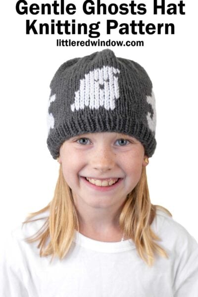 Cute girl wearing a gray knitted ghost hat with white pumpkin design for fall or Halloween.