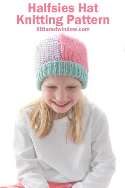 Smiling girl in white shirt and pink pants wearing a knit hat that has a light teal ribbed brim and is half pink stockinette stitch on the right and half light purple seed stitch on the left
