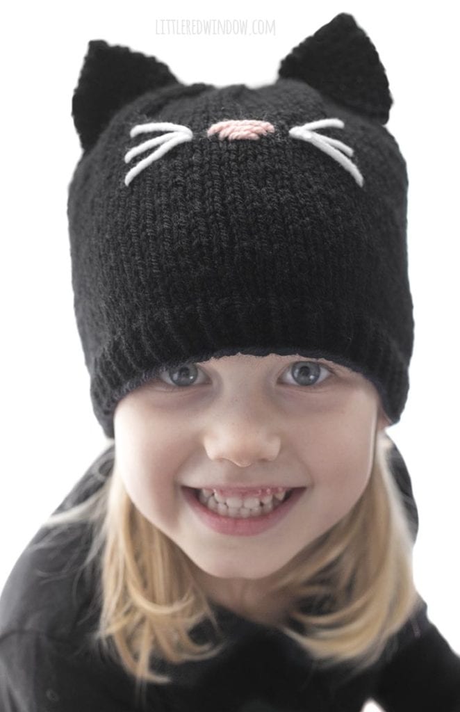 little girl looking up and smiling wearing a black shirt and knit black cat hat