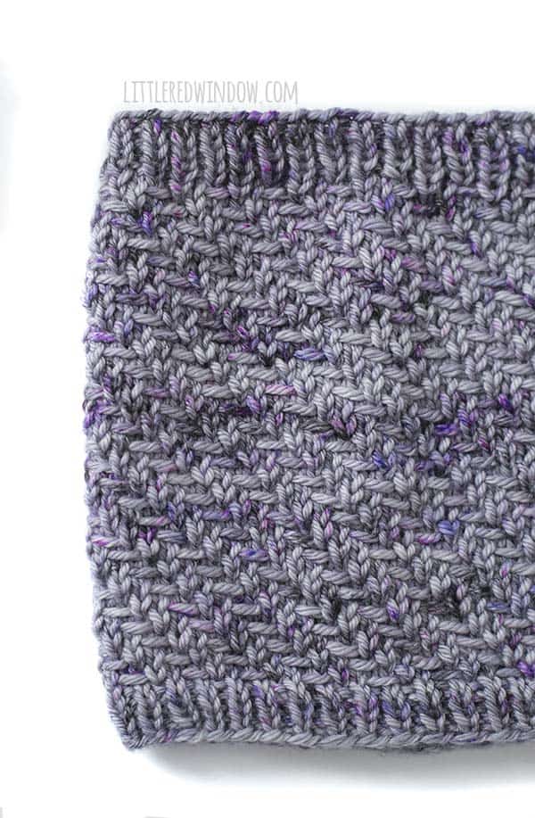 Closeup of the herringbone stitches on the hazel herringbone cowl in shades of lavender and purple yarn in front of a white background