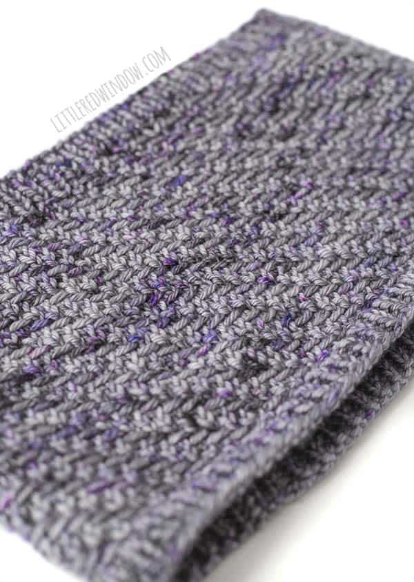 Closeup of the herringbone stitches on the hazel herringbone cowl laying flat diagonally in shades of lavender and purple yarn in front of a white background
