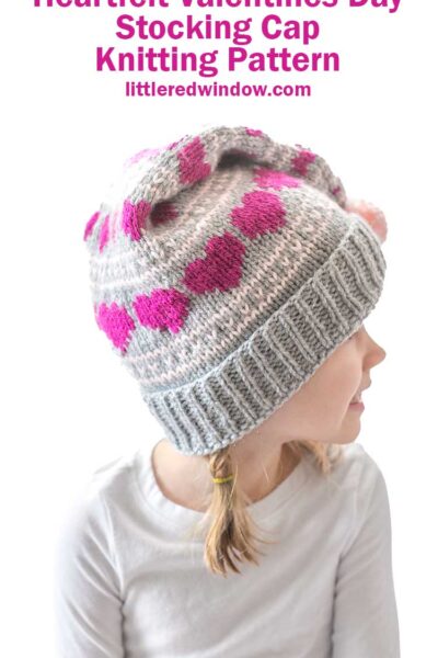 Young girl wearing a gray and pink knit stocking cap with heart patterns, looking to the side. Text reads: "Heartfelt Valentines Day Stocking Cap Knitting Pattern littleredwindow.com.