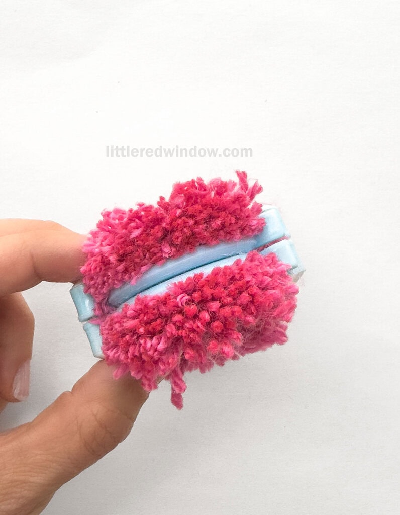 Using the sharpest scissors you can find, and keeping the pom pom maker closed, cut along one edge of one half the pom pom between the gap between the arches, all the way through all of the wrapped layers of yarn.