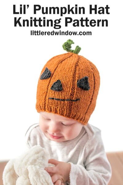 A baby wearing a knitted orange Pumpkin Hat resembling a jack-o'-lantern, complete with a green stem on top. The hat has black triangle eyes, a nose, and a jagged mouth. Text above the baby reads "Lil' Pumpkin Hat Knitting Pattern" and "littleredwindow.com".