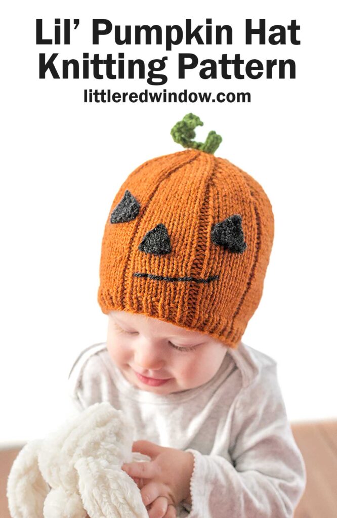 A baby wearing a knitted orange Pumpkin Hat resembling a jack-o'-lantern, complete with a green stem on top. The hat has black triangle eyes, a nose, and a jagged mouth. Text above the baby reads