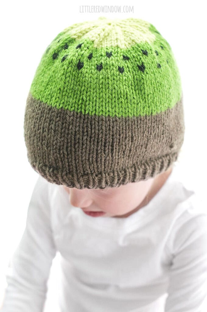 little girl modeling kiwi hat knitting pattern and wearing a white shirt
