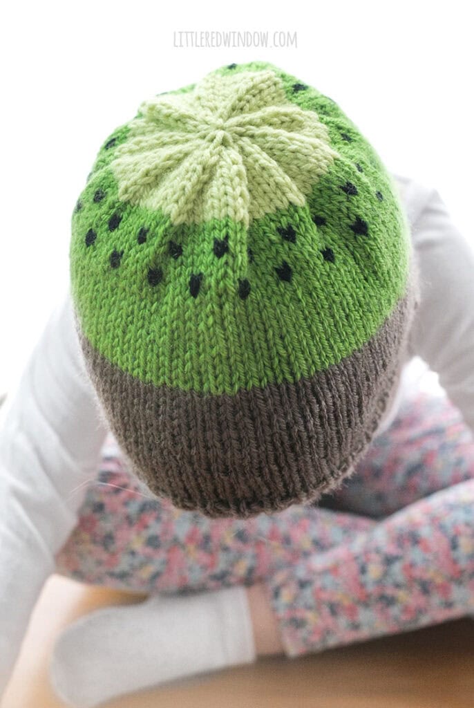 top view of small child wearing kiwi hat knitting pattern and leaning forward
