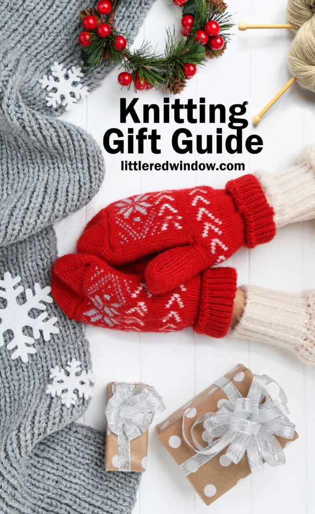 Hands in knitted mittens with grey scarf, snowflakes and gift boxes on white wooden table and the words knitting gift guide