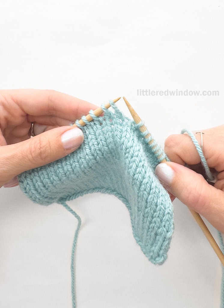 hands holding a light blue stockinette swatch in progress in front of a white background