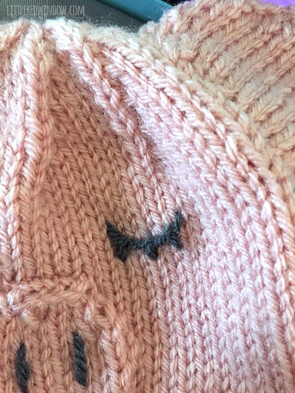 Close up of embroidered eye with eyelashes on pink knit pig hat