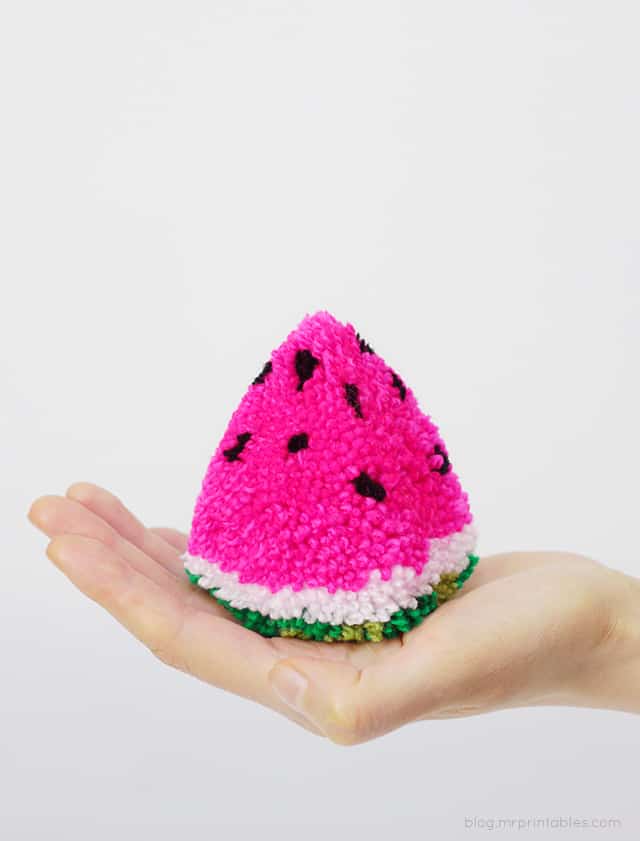 hand holding a green white and pink wedge shaped yarn pom pom