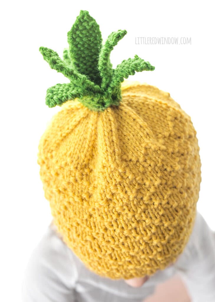 view from slight above of child wearing a knit pineapple hat with yellow diamond texture and green knit pineapple leaves on top