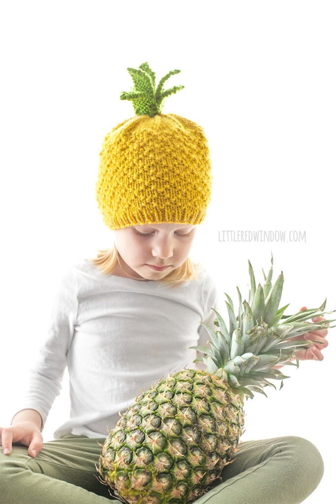 kid holding a pineapple and wearing a knit hat that looks like a pineapple
