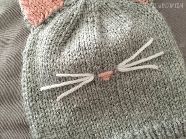 Finished front of knit cat hat with pink nose and white whiskers on the front