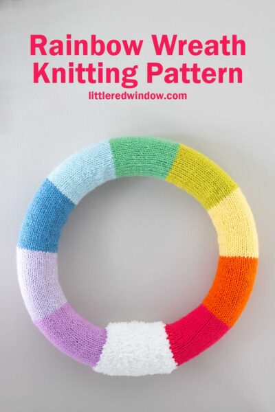 A colorful knitted wreath with rainbow segments: red, orange, yellow, green, blue, and purple. Text at the top reads "Rainbow Wreath Knitting Pattern" and "littleredwindow.com.