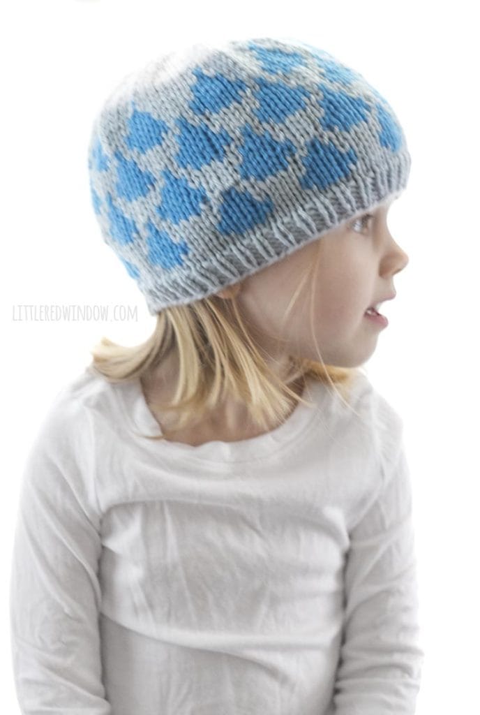 little girl wearing light blue knit hat with blue raindrop pattern and white cloud on top look off to the right