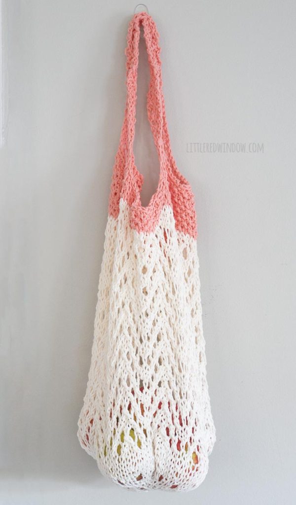 cream and coral lace knit market bag filled with apples hanging on a hook in front of a gray wall