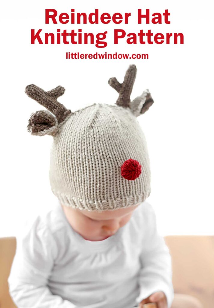 A baby in a reindeer hat with antlers and a red pom-pom nose is looking down, dressed in white. The text above reads, 