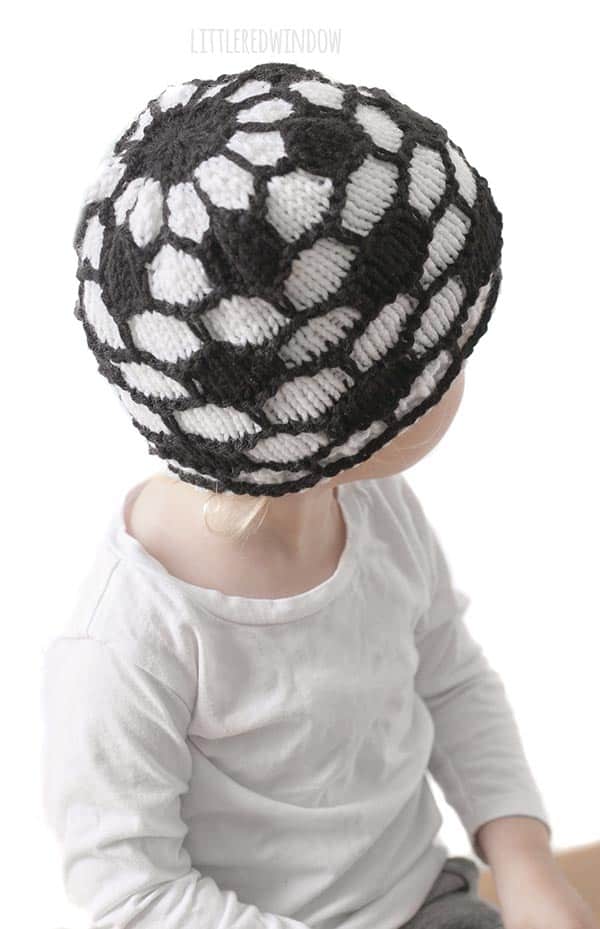 girl in white shirt wearing a knit hat that looks like a soccer ball and looking back over her left shoulder