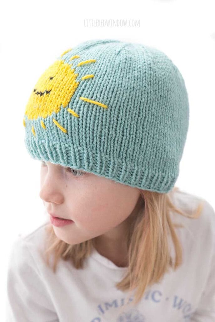 closeup side view of child with blonde hair wearing a sky blue and yellow sunshine hat and looking to the left