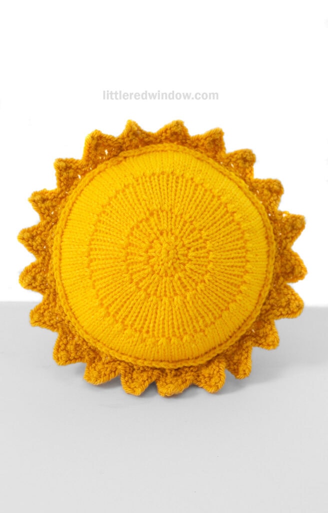 Propped up bright yellow knit sun shape in front of a white background