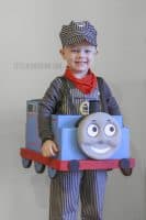 Smiling little boy wearing a train engineer costume and wearing the cardboard Thomas the Train costume!
